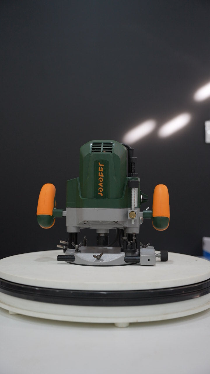 A green and gray JADEYER plunge router with orange side handles, displayed on a white circular platform against a dark gray background.