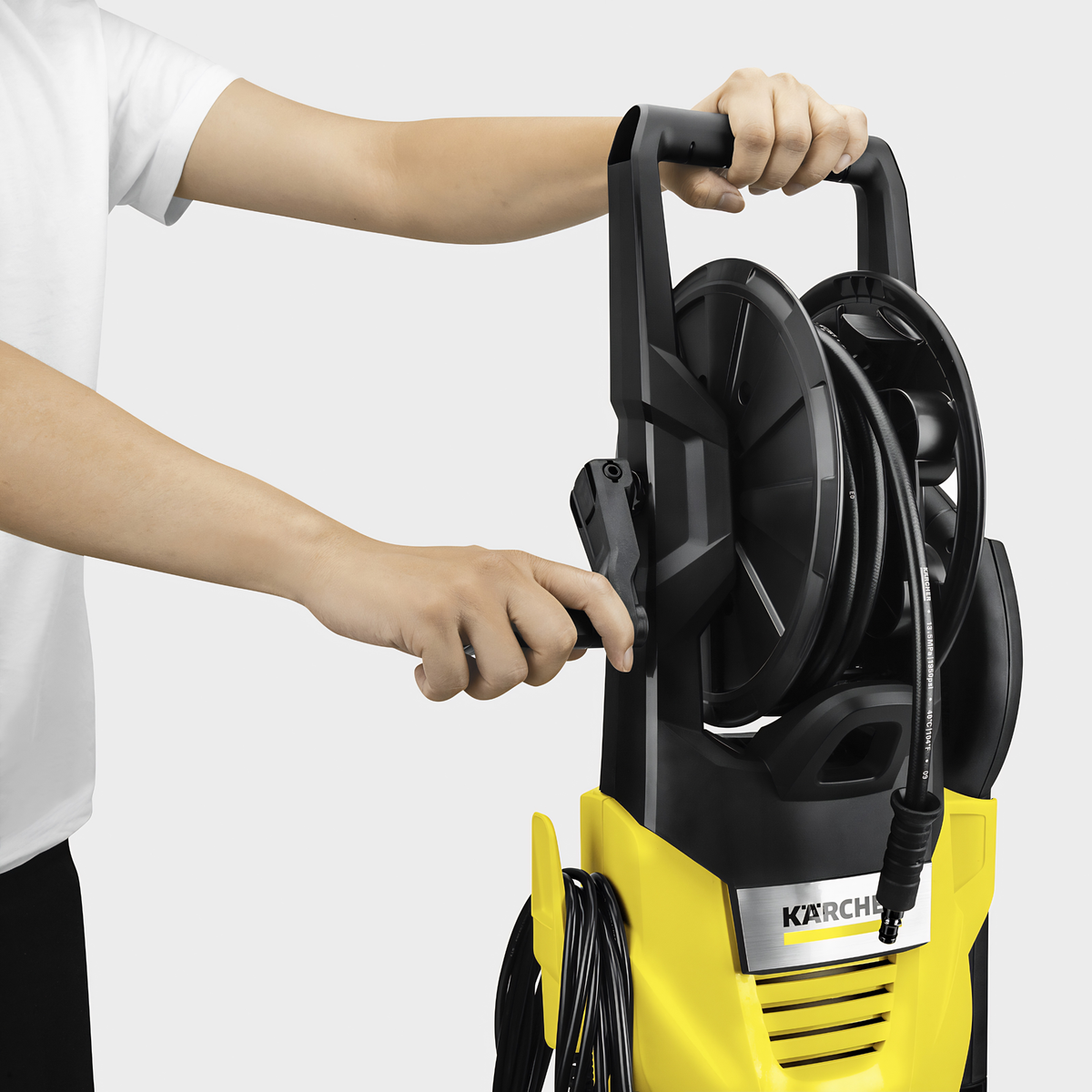 Person holding a Karcher pressure washer with coiled hose on a white background