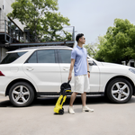 Man standing next to a white SUV holding a yellow robot-like device.