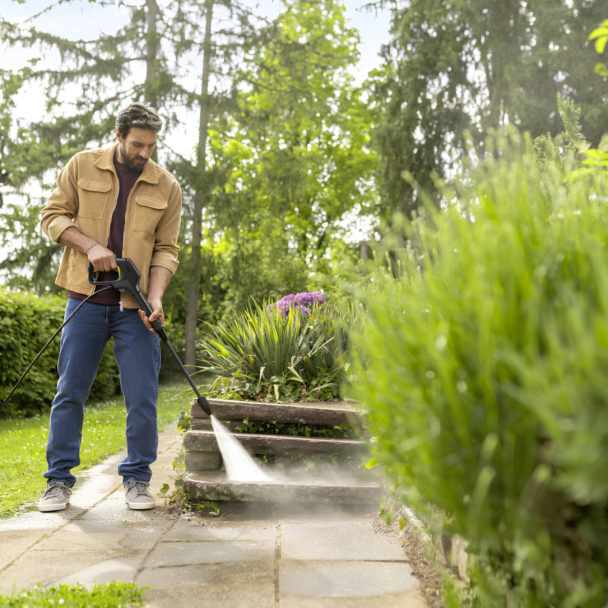 Man using a pressure washer on stone steps in a garden
