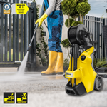 Person using a yellow pressure washer with a hose, wearing blue pants and yellow boots, in an outdoor setting.
