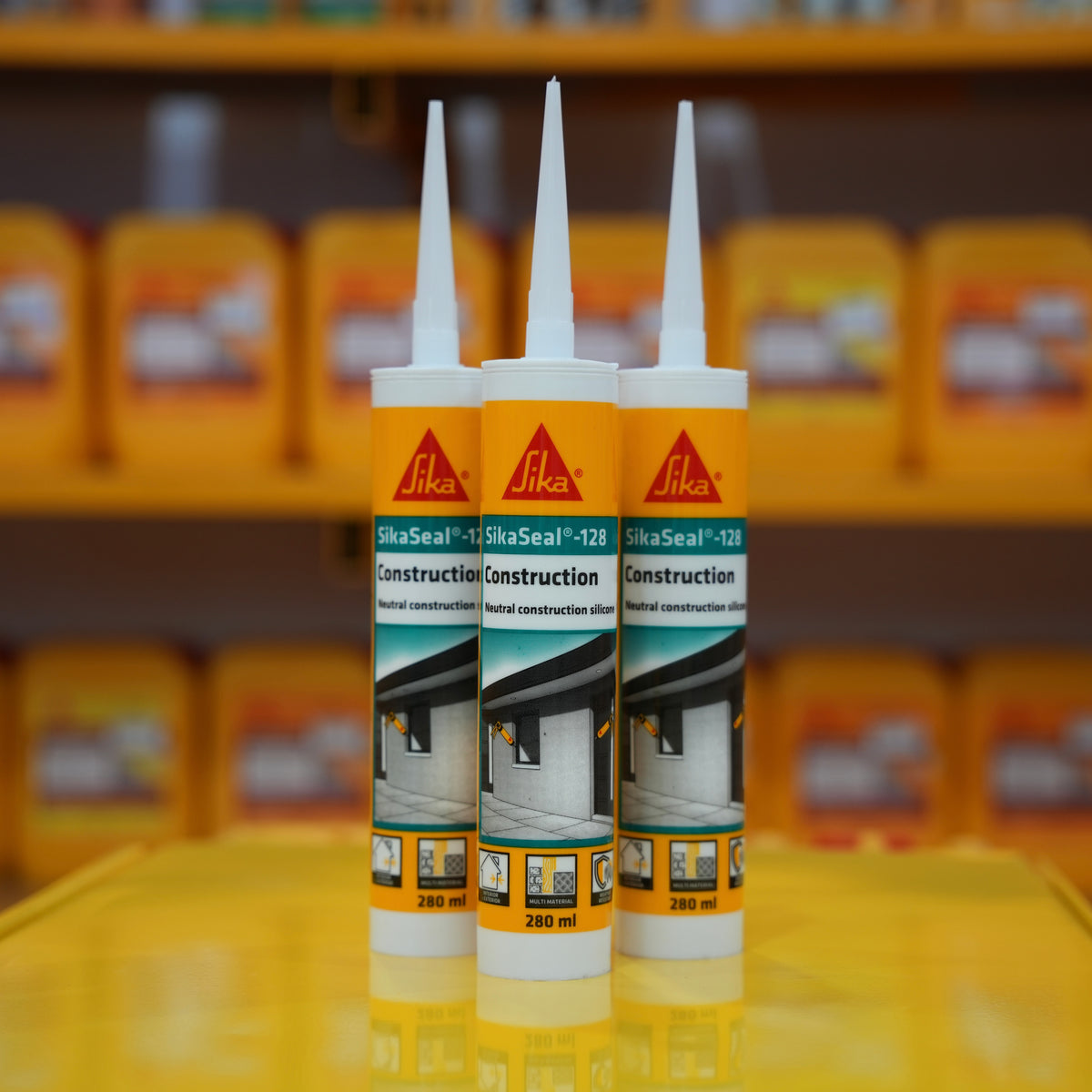 Two tubes of Sika construction sealant in front of shelves with more sealant bottles.