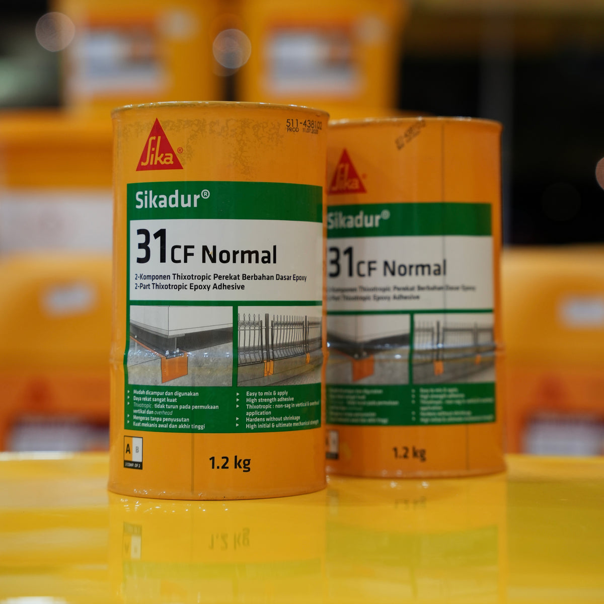 Two cans of Sikadur 31CF Normal epoxy adhesive on a reflective surface with blurred background