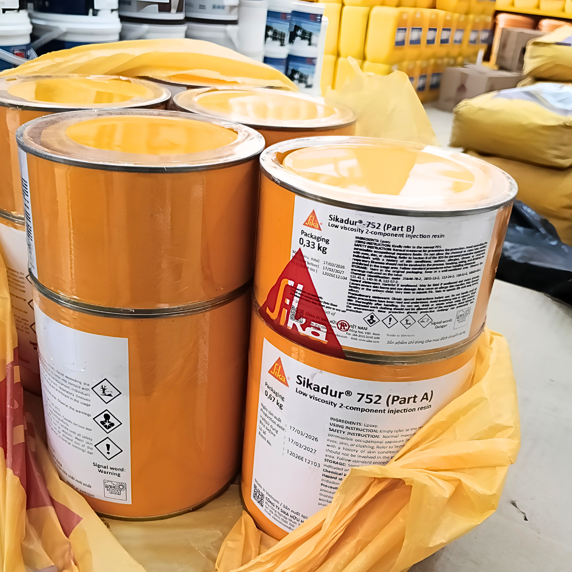 Two large orange Sika containers with labels on a warehouse floor.